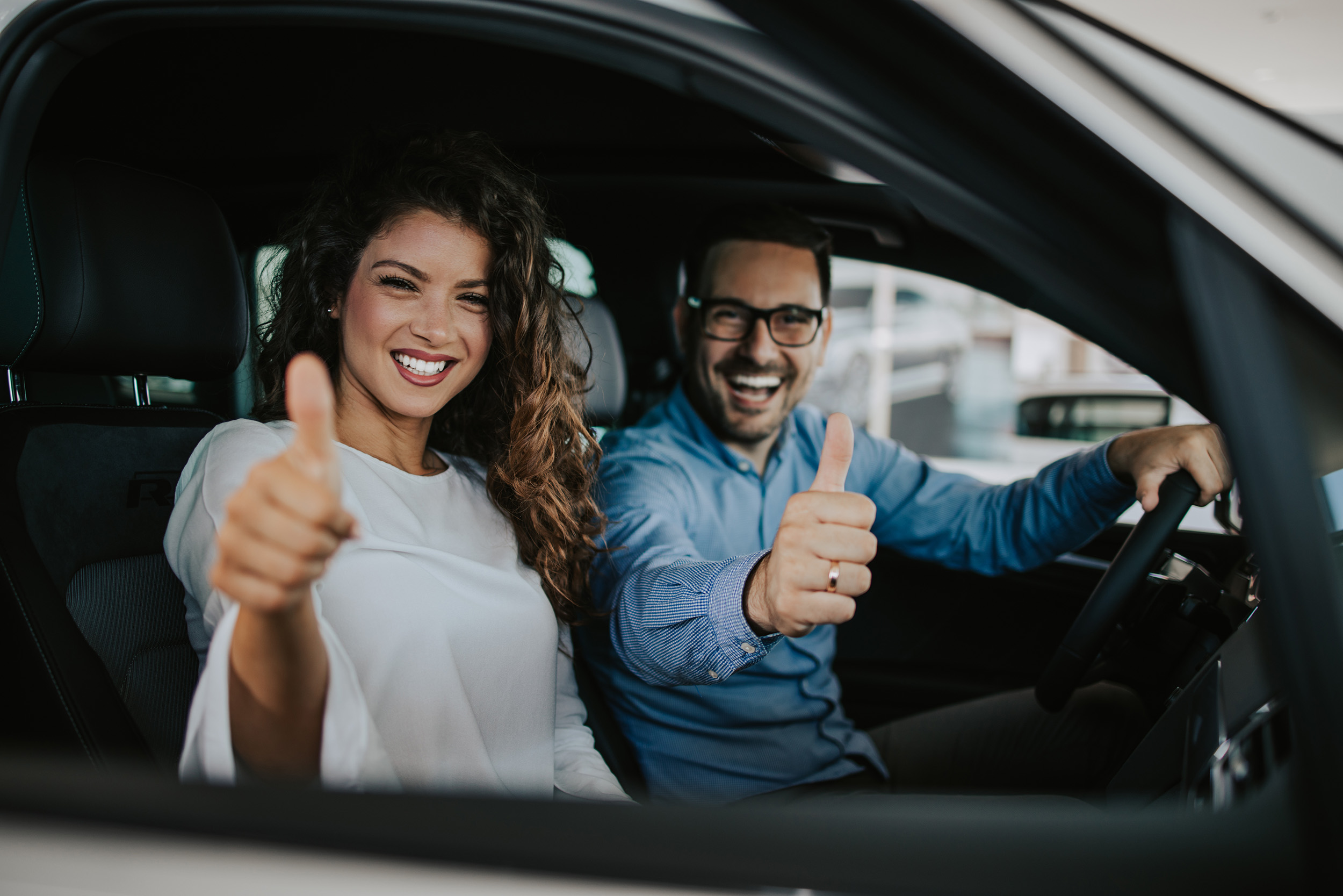 man and woman giving thumbs up from inside new car